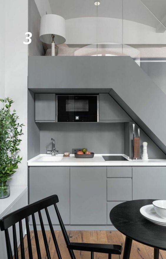 a laconic grey kitchen built in under the stairs, with white countertops and a small dining zone is all you need for a small home