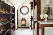 a large attic closet with open shelves and railings, with a round window and a chair and some lovely decor is all cool