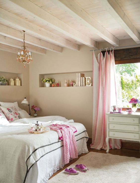 a lovely Provence bedroom with a low ceiling with beams, a niche for decor, a bed, a vintage dresser and a chandelier