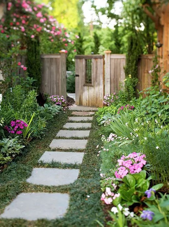 a lovely flourishing side yard with a green lawn, lots of greenery and bright blooms is a cool secret garden space