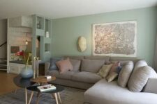 a lovely living room with pale green walls, a grey sectional with pillows, an arrangement of coffee tables and stools