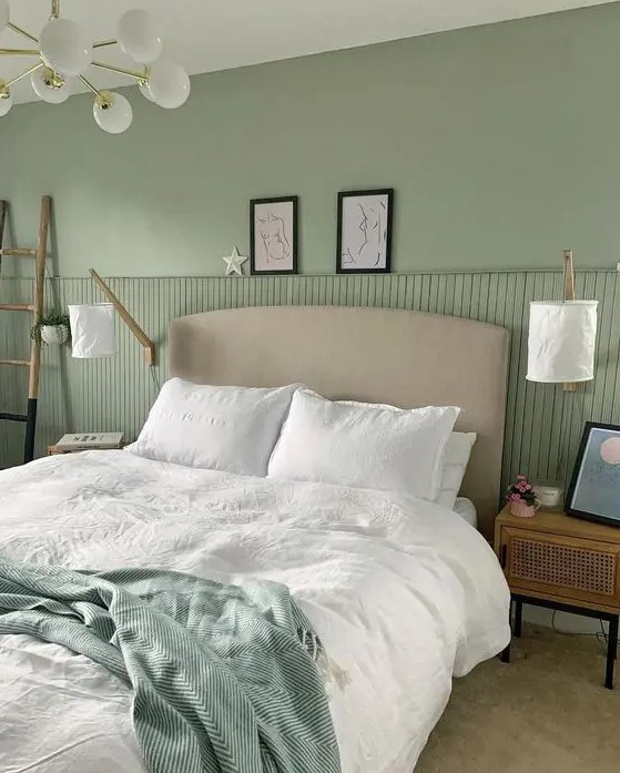 a lovely sage green bedroom with a grey bed and green and white bedding, cane nightstands, a ladder and sconces