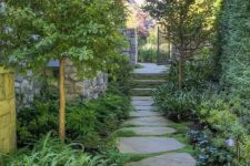 a lush and beautiful side yard with an irregular stone path, greenery and grasses and some trees plus lights along the path