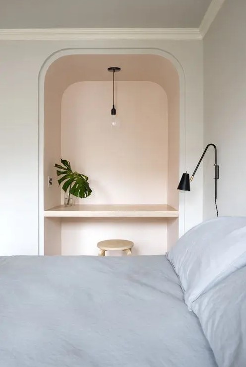 a minimal bedroom with a colored arched niche that is used as a tiny workspace or a vanity for makeup, with a pendant lamp