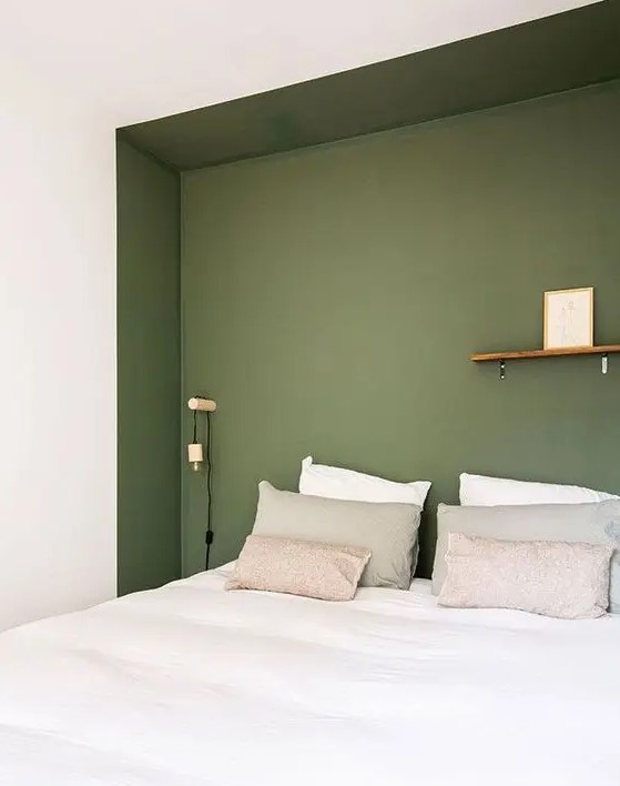 a minimal bedroom with a niche painted green, a bed in it, some sconces and a ledge for decorating