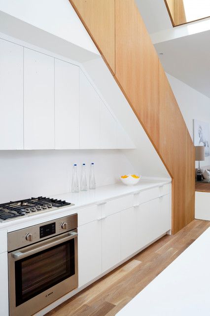 a minimalist white kitchen built right under the staircase, with a white kitchen island, a cooker and a white backsplash