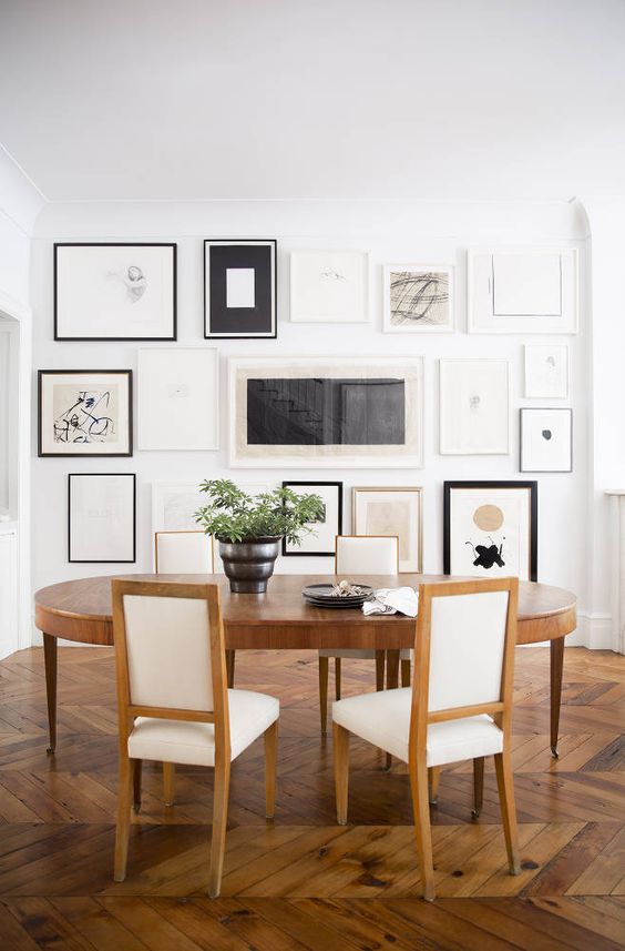 a modern and refined dining room with an oval table and neutral chairs, a floor to ceiling gallery wall with monochromatic artwork