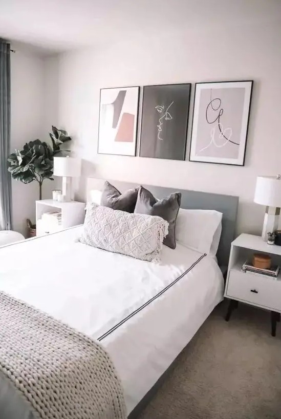 a modern and welcoming bedroom with a grey bed and neutral bedding, white nightstands, a small gallery wall and a potted plant