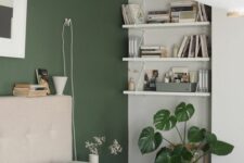 a modern bedroom with a green accent wall, a neutral bed and bedding, suspended shelving and a potted plant
