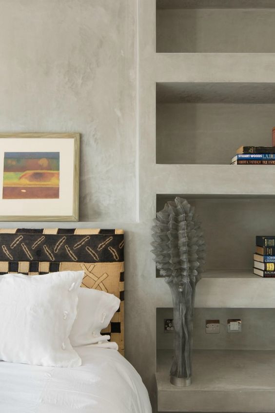 a modern bedroom with a series of niches for books and a quirky lamp, a bed with neutral bedding and some art