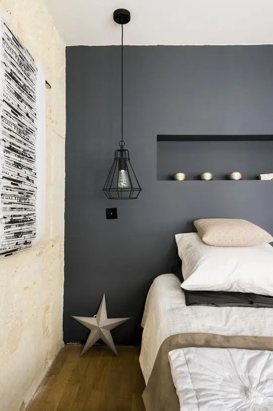 a modern bedroom with a soot accent wall and a niche with decor, a bed with neutral bedding, black pendant lamps