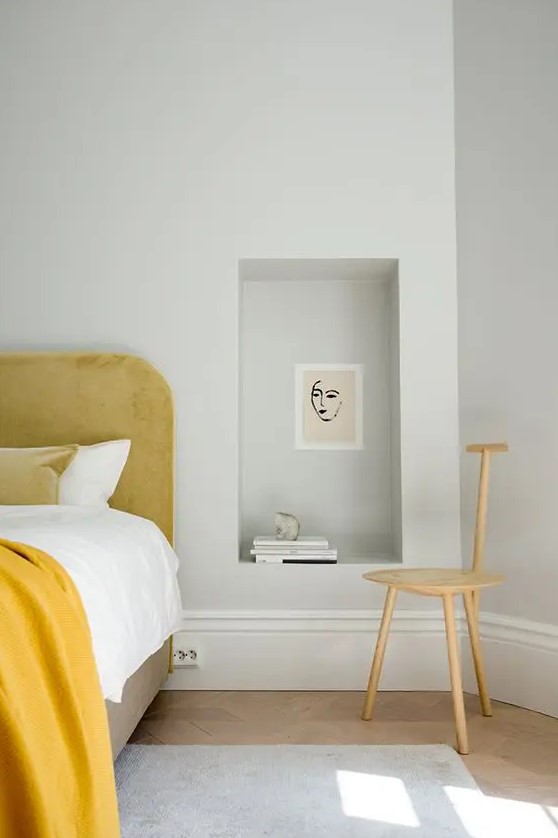 a modern bedroom with a yellow upholstered bed and bedding, a niche used as a nightstand and a whimsical chair is a lovely space