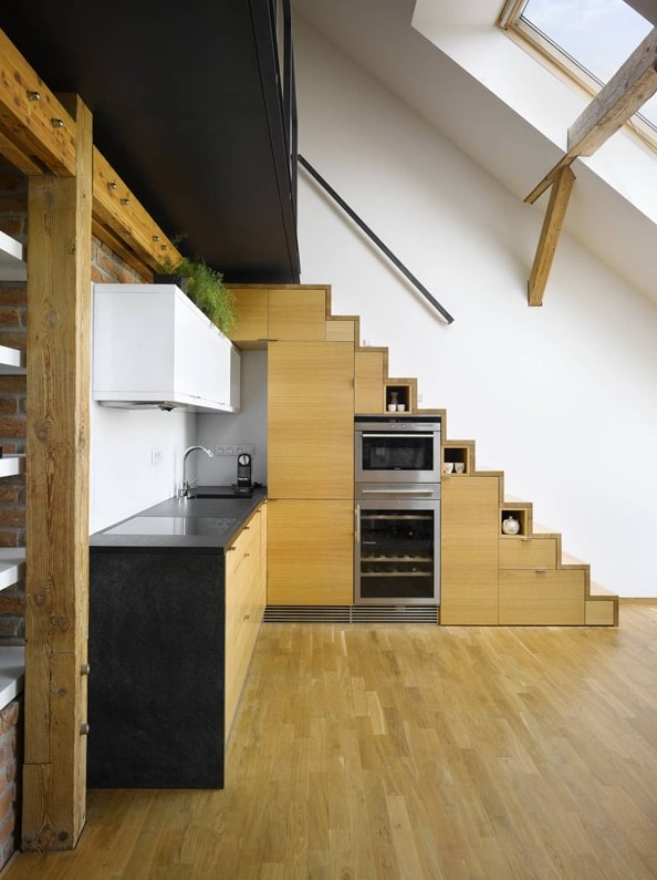 a modern contrasting kitchen with a stained timber staircase that includes cabinets, more cabinets in timber and white and black countertops