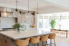 a modern country kitchen in dove grey, with shaker style cabinets, a large kitchen island, pendant lamp, woven stools