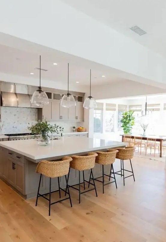 a modern country kitchen in dove grey, with shaker style cabinets, a large kitchen island, pendant lamp, woven stools