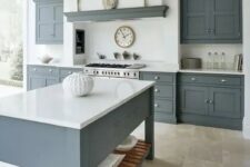 a modern country kitchen with graphite grey cabinets and a kitchen island, white countertops and a built-in hood plus a glazed wall