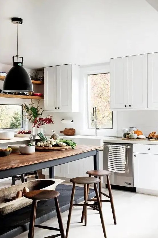 a modern country kitchen with white cabinetry and a black kitchen island plus a butcherblock countertop and black pendant lamps