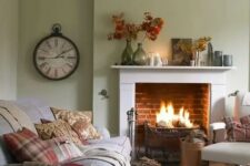 a modern country living room with light green walls, a fireplace, neutral furniture and printed textiles, a vintage clock and leaves