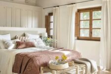 a modern farmhouse bedroom in neutrals, with a large wardrobe, a neutral bed with muted bedding, a woven bench and a printed rug