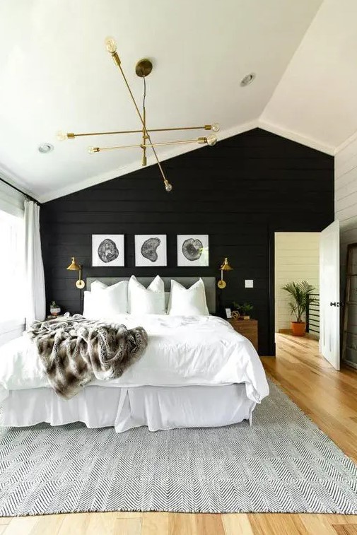 a modern farmhouse bedroom with a black accent wall, a grey upholstered bed with neutral bedding, a mini gallery wall, a gold chandelier
