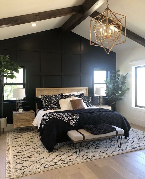 a modern farmhouse bedroom with a black paneled wall, a bed with black and white bedding, nigthstands, a bench and a geo lamp