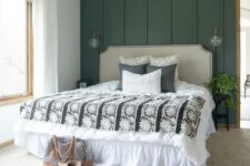 a modern farmhouse bedroom with a dark green accent wall, a neutral upholstered bed, layered rugs and some greenery