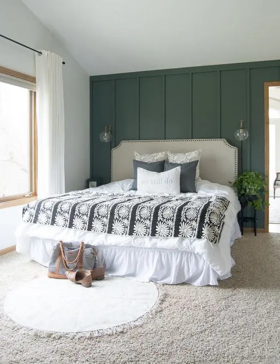 a modern farmhouse bedroom with a dark green accent wall, a neutral upholstered bed, layered rugs and some greenery