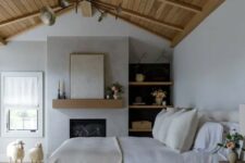 a modern farmhouse bedroom with a fireplace, a wooden ceiling, open shelves, a bed with neutral bedding, a fluffy rug