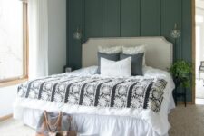 a modern farmhouse bedroom with a green paneled wall, a neutral bed with printed bedding, layered rugs and sconces