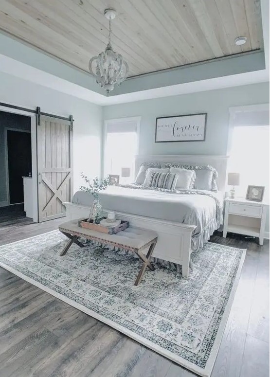 a modern farmhouse bedroom with white furniture, an upholstered bench, a vintage chandelier and ruffle bedding
