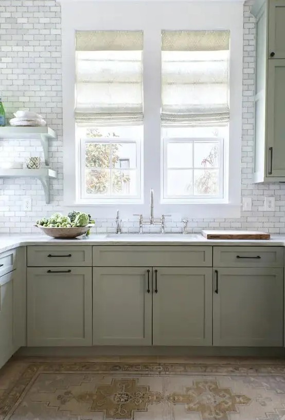 a modern farmhouse kitchen in sage green, with shaker cabinets, white stone countertops, white marble tiles and vintage fixtures