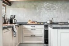 a modern farmhouse kitchen with neutral shaker cabinets, black stone countertops, a pale green zellige tile backsplash