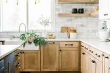 a modern farmhouse kitchen with white and stained cabinets, a black kitchen island, corner shelves and a marble tile backsplash