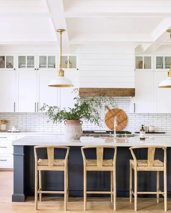 a modern farmhouse kitchen with white cabinets, a soot kitchen island, pendant lamps, woven stools and touches of wood