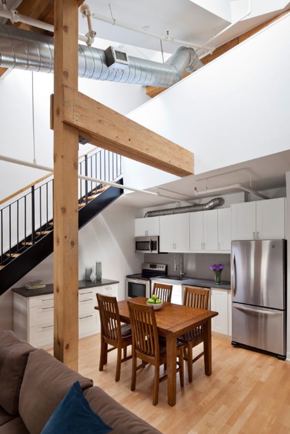 a modern kitchen with white cabinets and black countertops placed under the stairs, with a dining set of stained wood