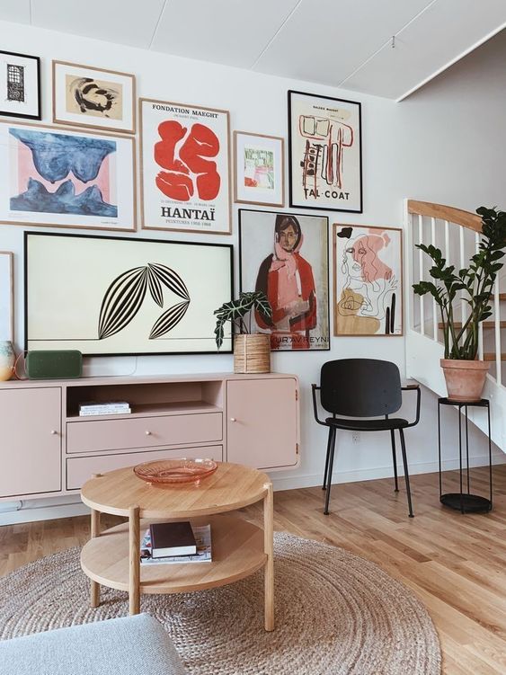 a modern living room with a free form gallery wall, a pink sideboard, a black chair and a plant stand, a wooden coffee table