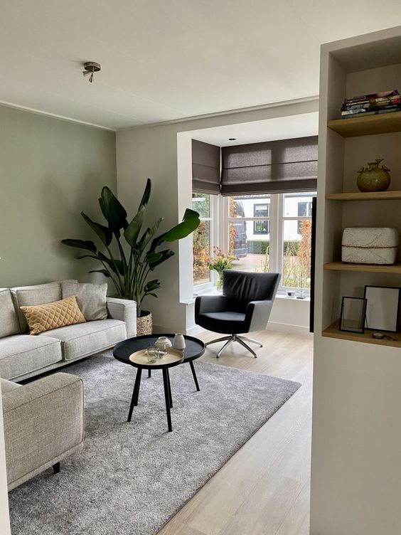 a modern living room with an olive green accent wall, a grey sectional, a black coffee table, and a chair and some storage units