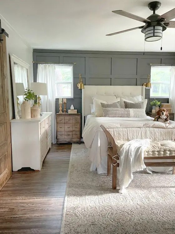a modern neutral bedroom with a grey paneled wall, a creamy upholstered bed with neutral bedding, stained nightstands and a white dresser