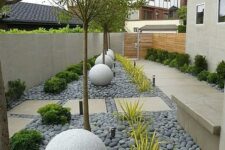 a modern side yard styled with tiles and grey pebbles, stone balls, trees, greenery and succulents is a stylish space that catches an eye