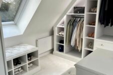 a modern white attic closet with open storage compartments and built-in lights, a storage ottoman and a dresser with a bench
