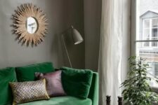 a moody living room with grey walls, a bold green sofa, a stained bench as a coffee table, a burst mirror and a taupe floor lamp