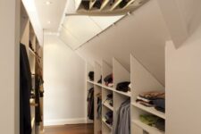 a neutral attic closet with open storage compartments and drawers, mirrors on the ceiling and built-in lights