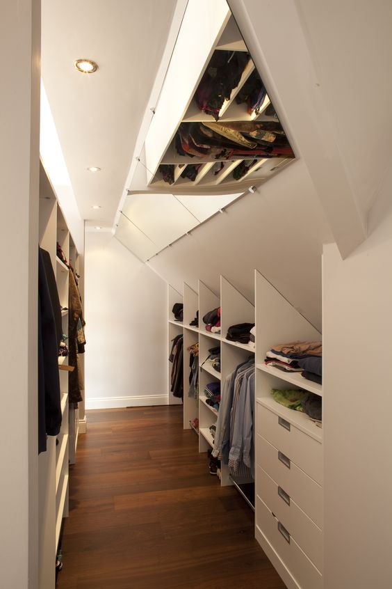 a neutral attic closet with open storage compartments and drawers, mirrors on the ceiling and built-in lights