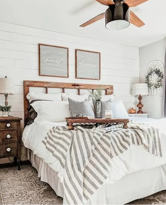 a neutral farmhouse bedroom with shabby wooden furniture, neutral and printed textiles, greenery and cool rustic lamps
