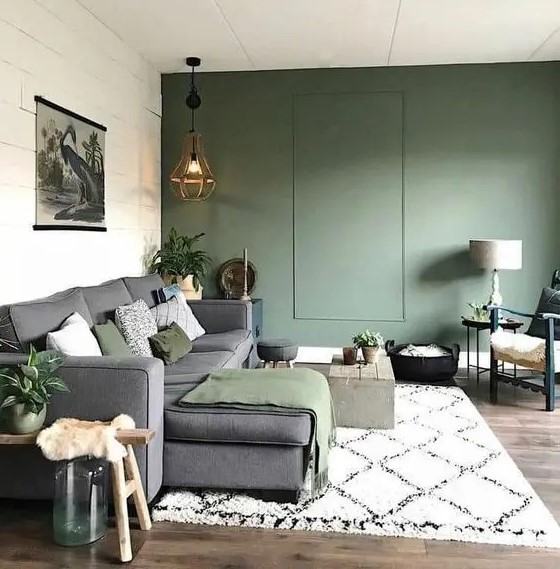 a neutral living room with a green accent wall, a grey sectional with green textiles, potted greenery and some lovely decor