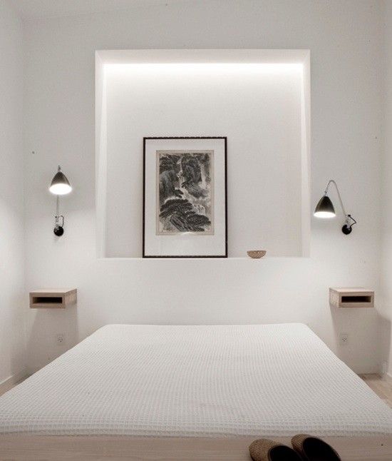 a neutral minimal bedroom with a large lit up niche, a bed, floating nightstands, black sconces