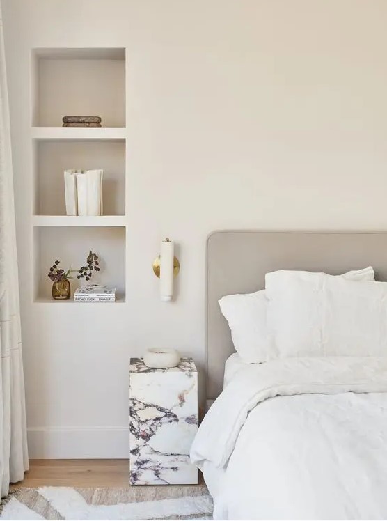 a neutral serene bedroom with a bed, a marble nightstand and niche shelves used fro storage and decor