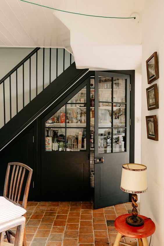 a pantry built in under the staircase, with elegant French doors and open shelves and railings inside is a perfect solution