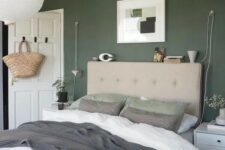 a peaceful Scandinavian bedroom with a dark green accent wall, a tan bed with green and white bedding, white nightstands and greenery