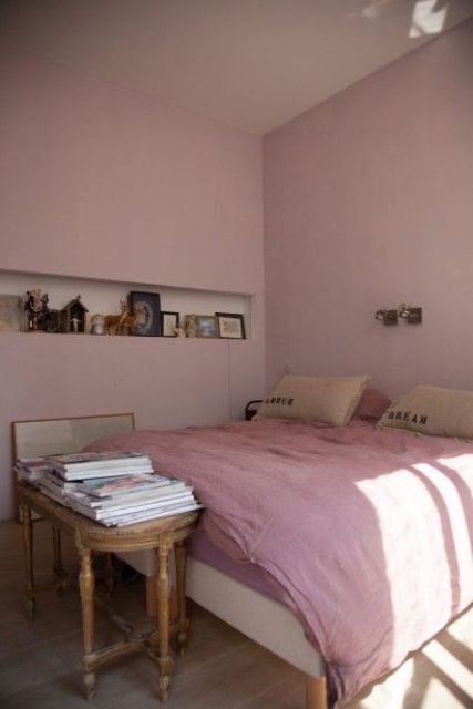 a pink bedroom with a bed and pink bedding, a niche for decor, a vintage coffee table with books and a mirror